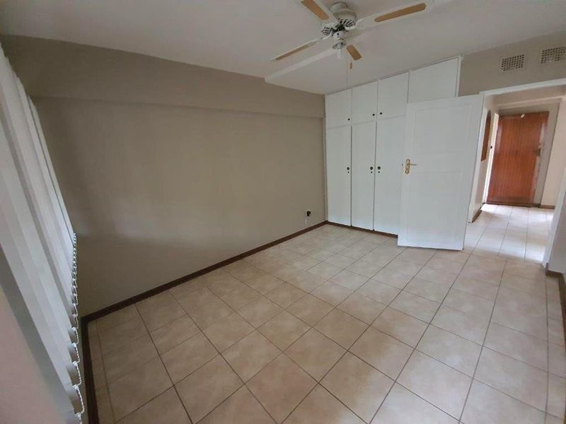 A spacious, empty bedroom featuring neutral tiled flooring, built-in storage cupboards, and a ceiling fan, offering a clean canvas for personalization.