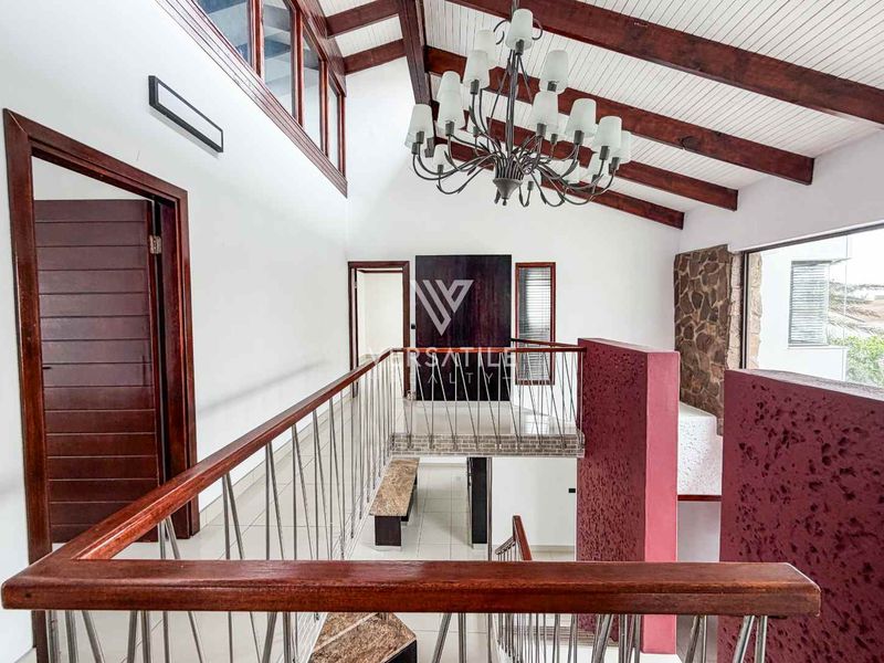 Spacious landing area featuring a vaulted ceiling with exposed timber beams, a stone feature wall, and a grand chandelier overlooking the staircase.