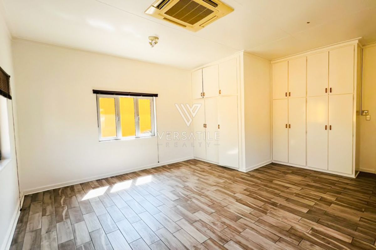 A spacious, empty bedroom featuring extensive built-in cupboards, tiled flooring, and a ceiling-mounted air conditioning unit.
