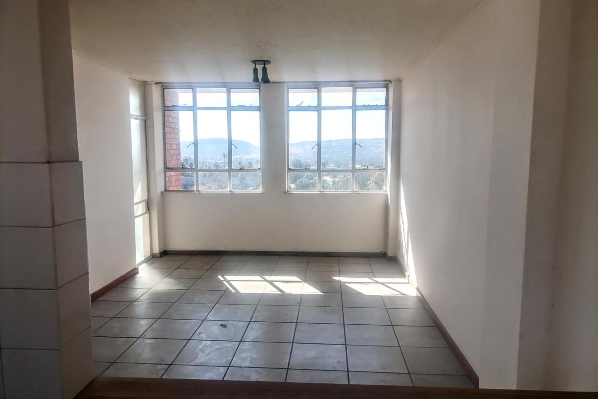 An empty, sunlit living area featuring tiled flooring, large windows with scenic views, and neutral walls, offering a blank canvas for renovation.