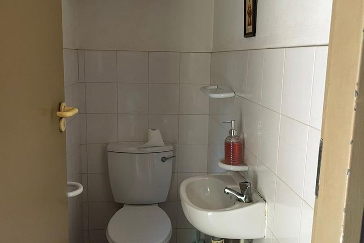 A compact guest bathroom featuring a wall-mounted basin and standard toilet with white wall tiling and terracotta-style floor tiles.