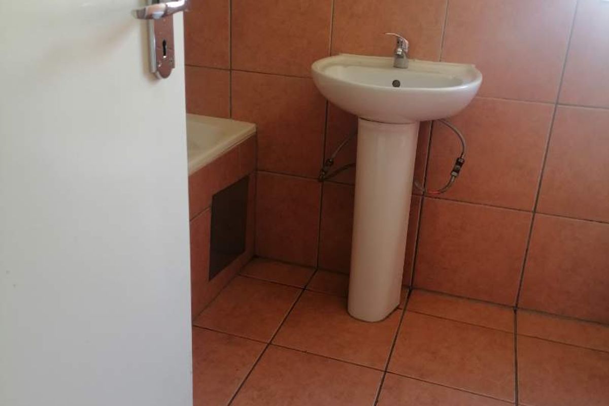 A dated bathroom featuring terracotta-style floor and wall tiles, a pedestal basin, and a built-in bathtub.