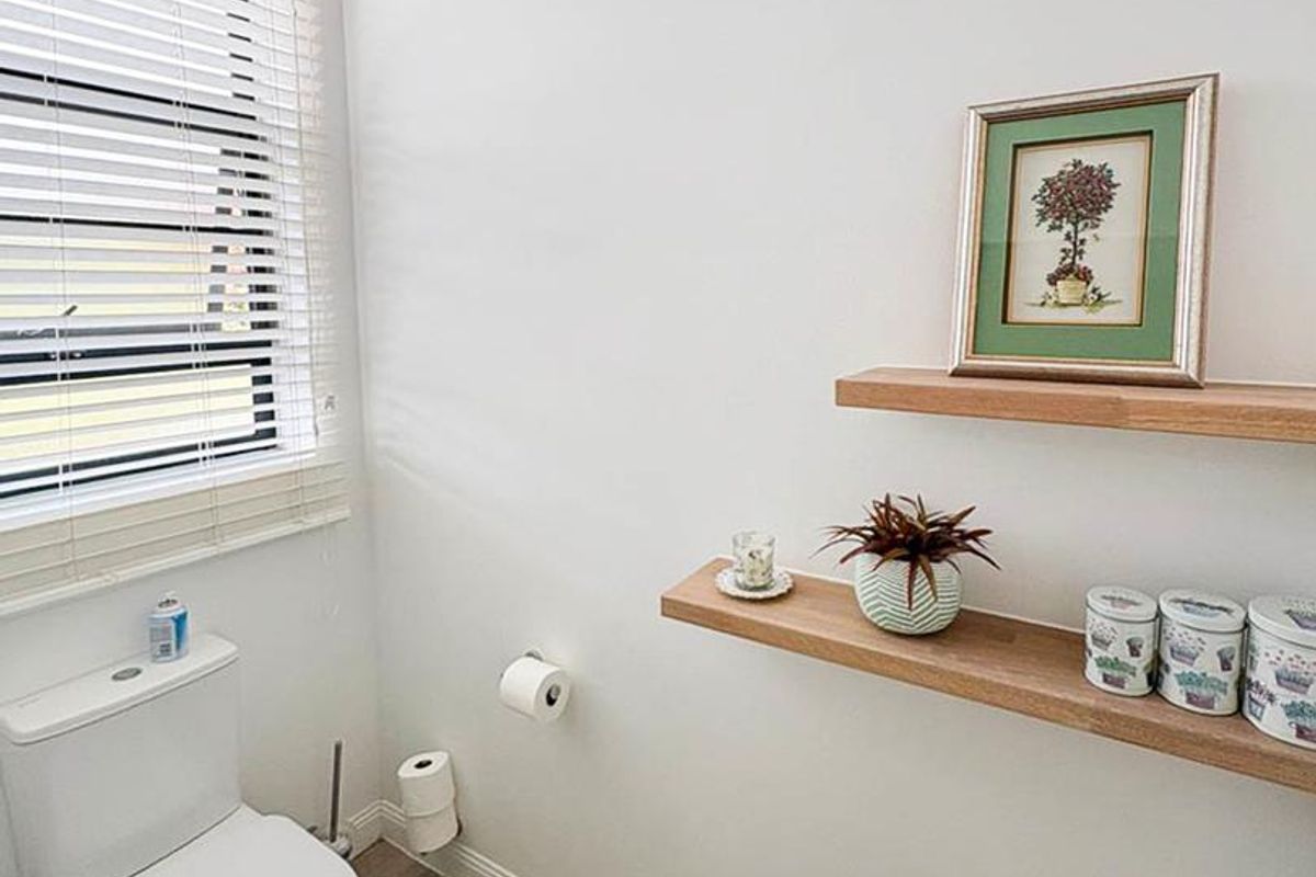 A clean and functional bathroom featuring a modern toilet, wood-look flooring, and built-in floating timber shelves.
