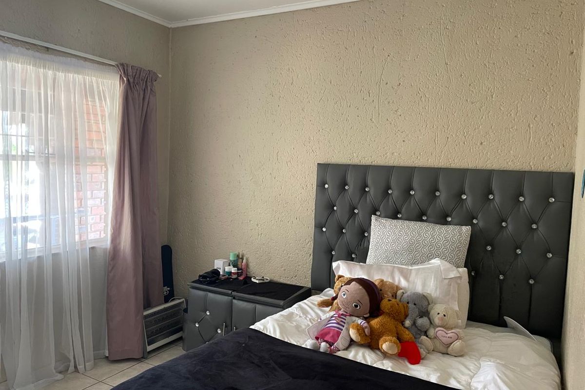 A bedroom featuring textured walls, tiled flooring, and a window with curtains, providing a functional space for rest.
