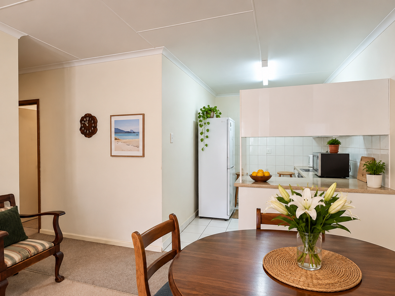 Open-plan living and dining area featuring a functional kitchen with built-in cabinetry, tiled splashback, and neutral finishes throughout.