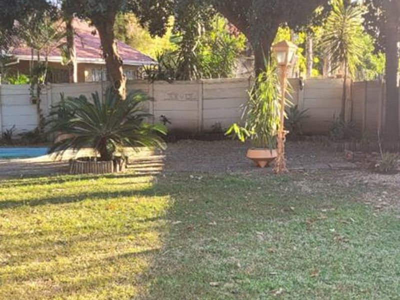 A spacious backyard garden featuring a well-maintained lawn, mature trees, and a secure precast concrete boundary wall.