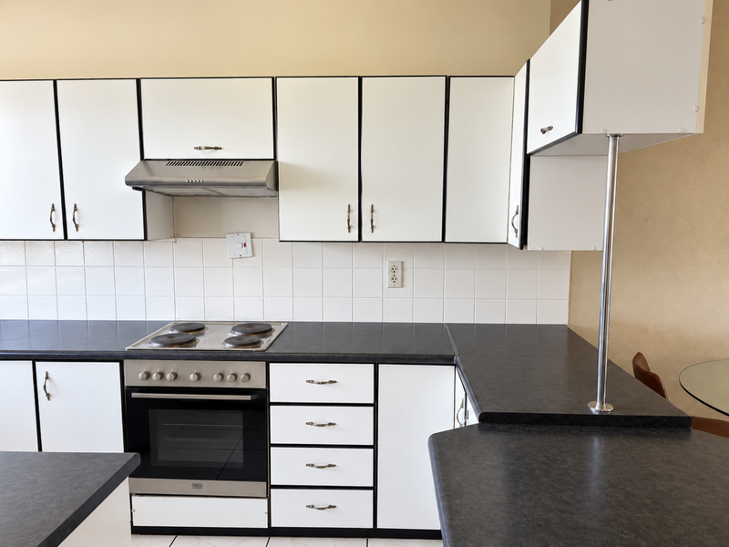 A functional kitchen featuring white cabinetry with black trim, dark laminate countertops, a built-in oven, electric hob, and a tiled backsplash.