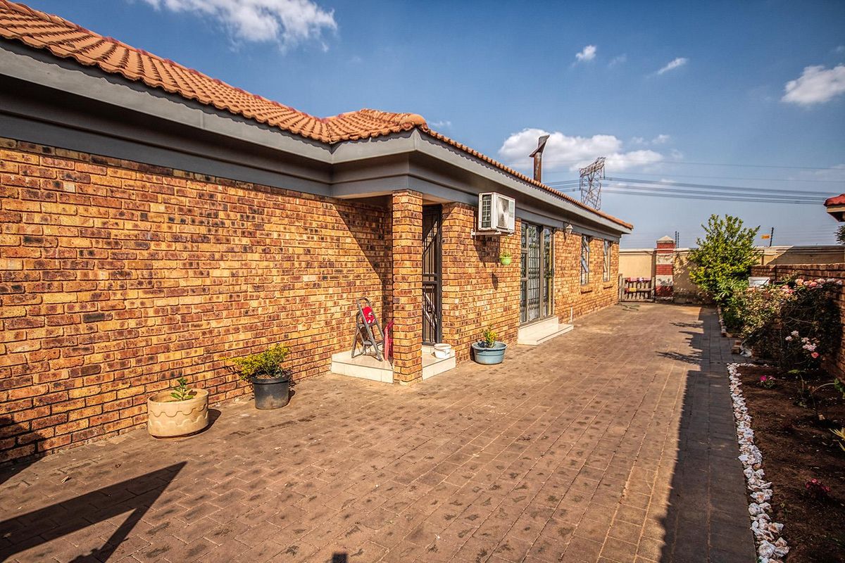 Rear exterior view of the house featuring a paved patio area, face-brick facade, and a wall-mounted air conditioning unit.