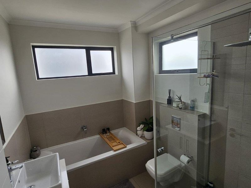 Modern bathroom featuring a built-in bathtub, wall-mounted toilet, glass-enclosed shower, and a contemporary vessel sink with neutral tiling.