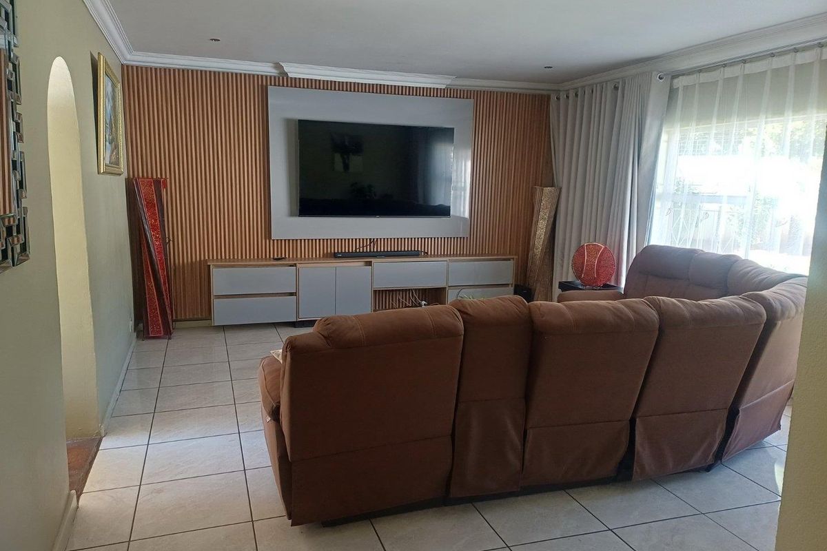 A comfortable living room featuring a built-in media wall with vertical slat paneling, tiled flooring, and large windows with curtains.