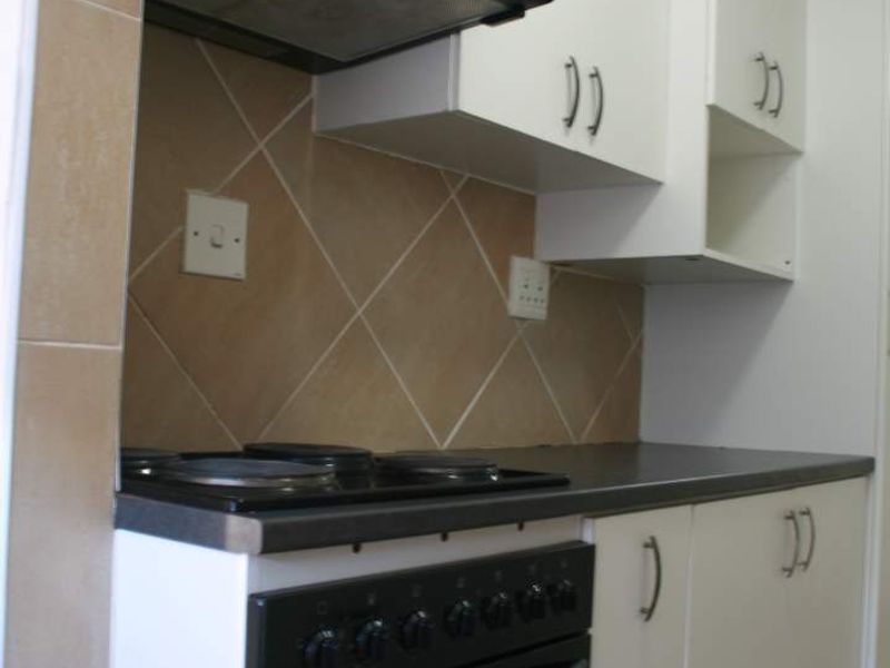 Compact kitchen featuring white cabinetry, dark laminate countertops, a built-in oven with electric hob, and a tiled backsplash.