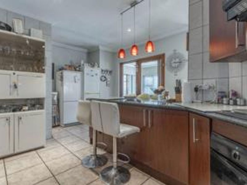 A functional kitchen featuring dark wood cabinetry, a central island with breakfast bar seating, tiled flooring, and modern pendant lighting.