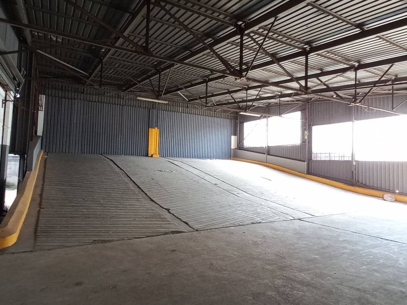 Spacious industrial loading bay featuring a large concrete ramp, high-clearance steel truss roof, and corrugated metal wall cladding.