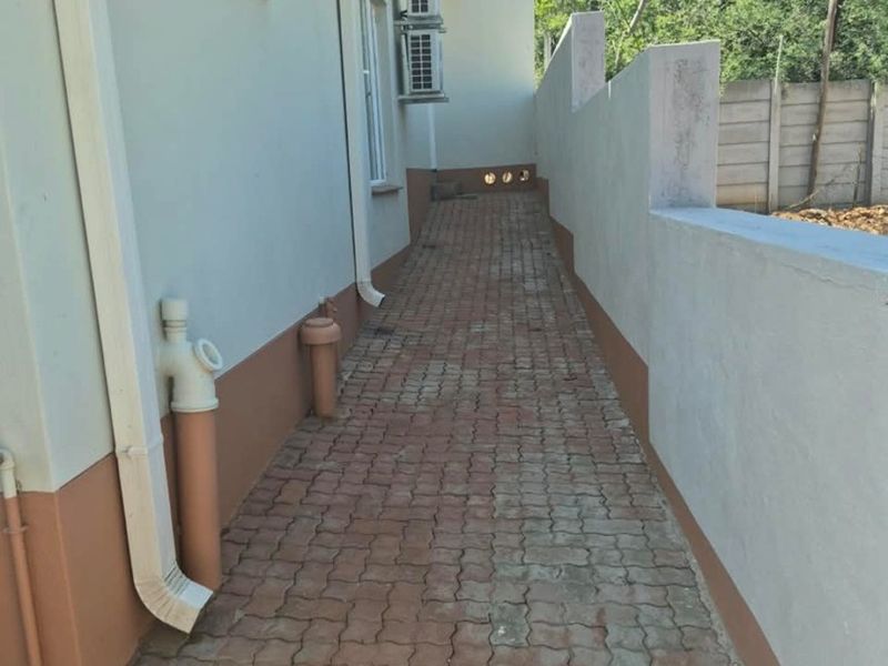A side exterior walkway featuring paved flooring, boundary wall, and mounted air conditioning units along the side of the house.
