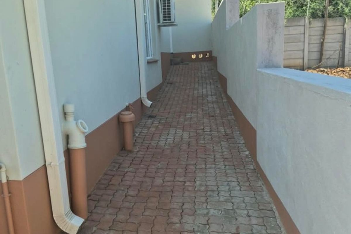 A side exterior walkway featuring paved flooring, boundary wall, and mounted air conditioning units along the side of the house.