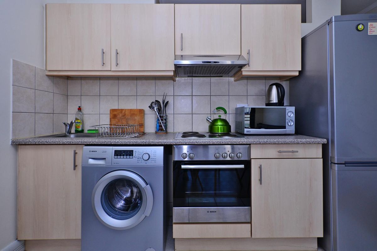 Compact kitchen featuring light wood-finish cabinetry, granite-look countertops, tiled backsplash, and integrated stainless steel oven and extractor fan.