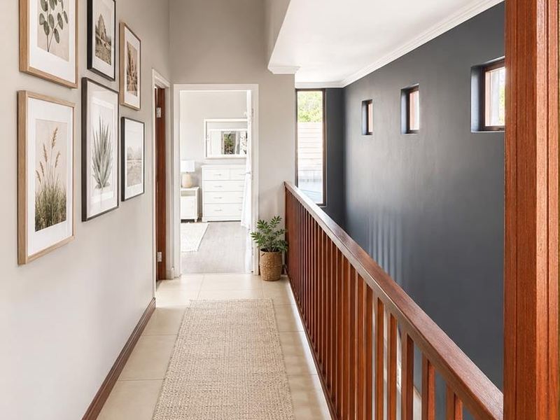 A bright and well-maintained upper-level hallway featuring a wooden balustrade, tiled flooring, and elegant crown molding, leading to adjacent bedrooms.