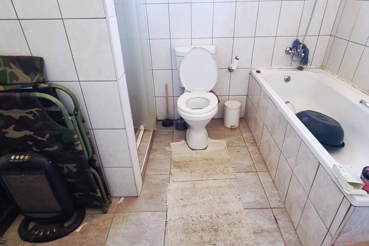 A functional bathroom featuring a standard bathtub, toilet, and full-height wall tiling. The space requires cosmetic updates to improve its overall condition.