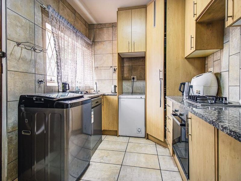 A functional kitchen featuring light wood cabinetry, granite countertops, a built-in oven, gas hob, and tiled finishes throughout.