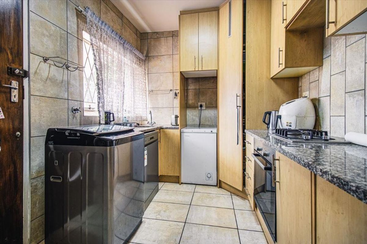 A functional kitchen featuring light wood cabinetry, granite countertops, a built-in oven, gas hob, and tiled finishes throughout.