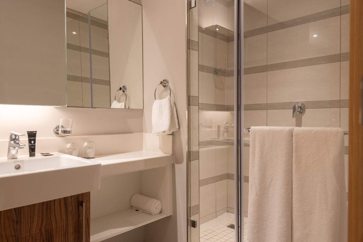 Modern bathroom featuring a vanity with integrated basin, wall-mounted mirror, and a glass-enclosed shower with neutral tiled finishes.