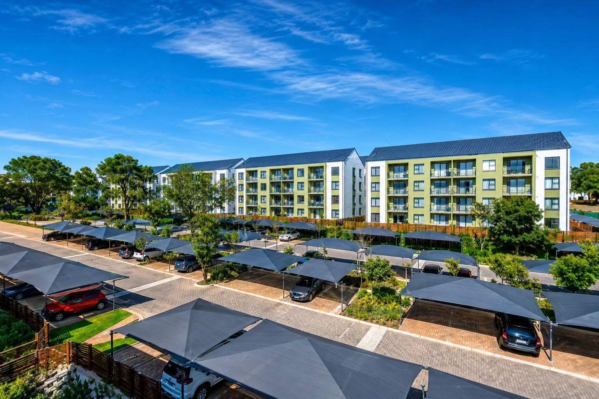 Aerial view of a modern apartment complex featuring multi-story residential buildings, paved parking areas with shade cloth carports, and landscaped grounds.