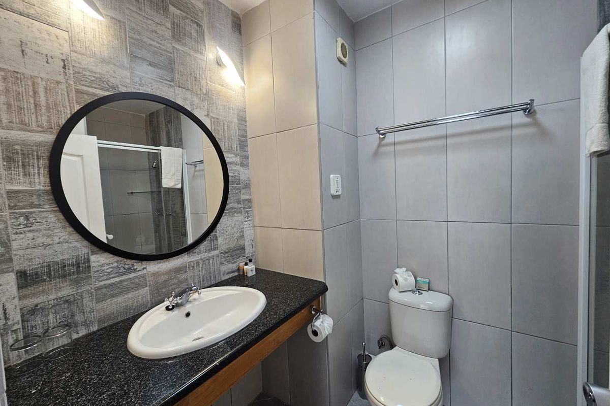 A modern hotel bathroom featuring a granite-topped vanity with an integrated basin, a wall-mounted toilet, and neutral-toned tiled walls.