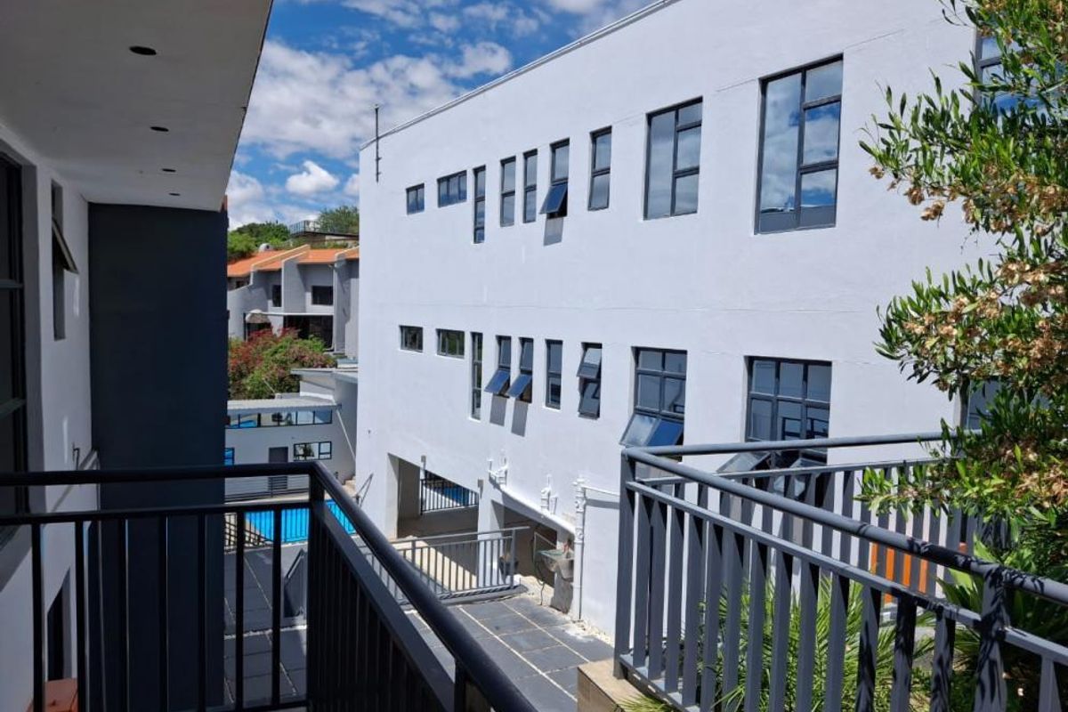 View from a balcony overlooking a paved courtyard and the rear facade of a modern multi-story residential building.