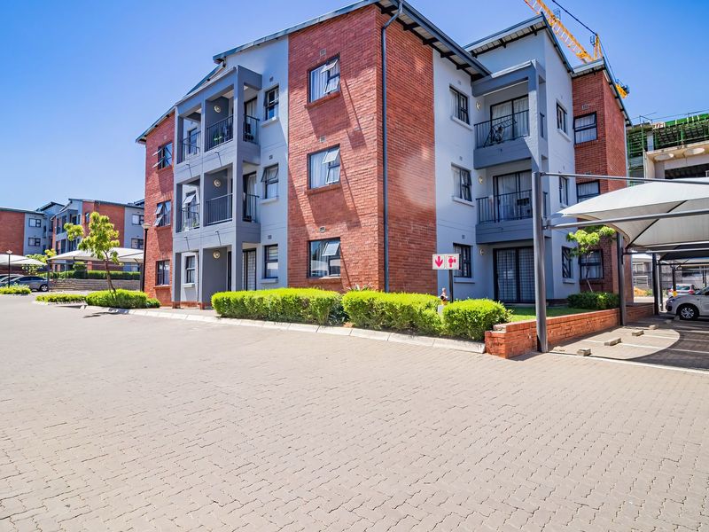 Exterior view of a modern multi-story apartment complex featuring brick and plaster facade, private balconies, and covered parking bays.