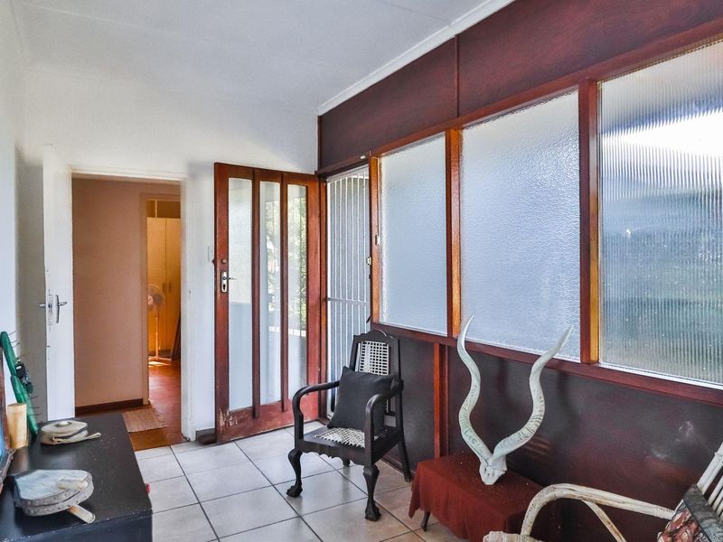 Enclosed patio area featuring tiled flooring, timber-framed glass doors, and ribbed glass windows, offering a versatile space with potential for modernization.