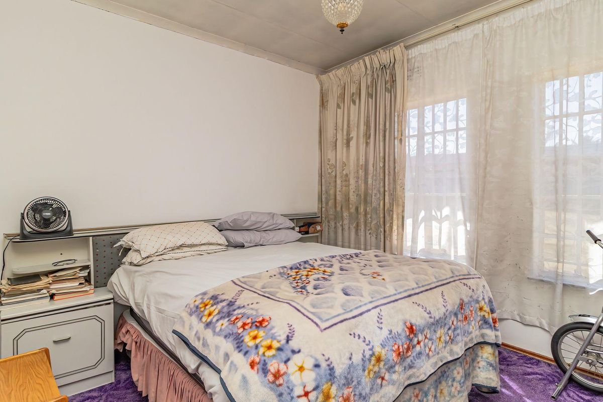 A bedroom featuring a built-in headboard, window with security bars, and carpet flooring, offering a functional space ready for cosmetic updates.