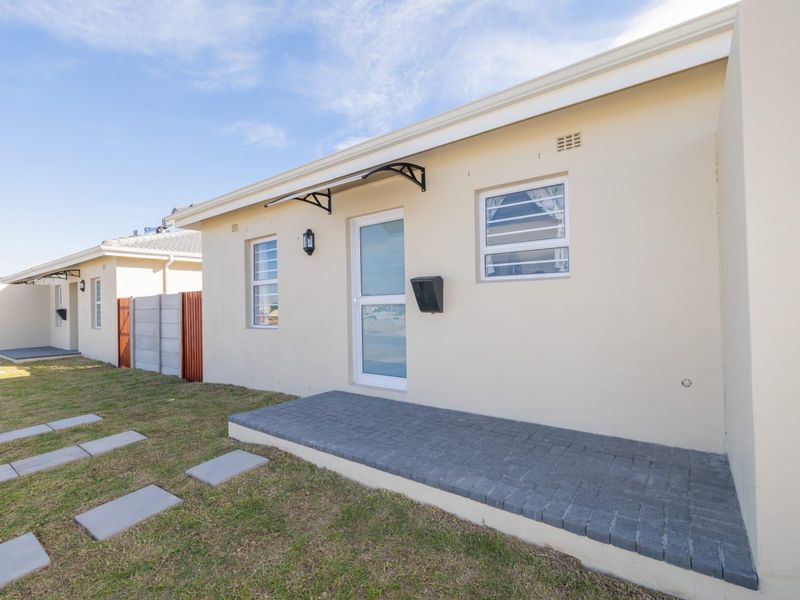 Front exterior view of a modern residential unit featuring a paved entrance, louvered windows, and a small awning over the front door.