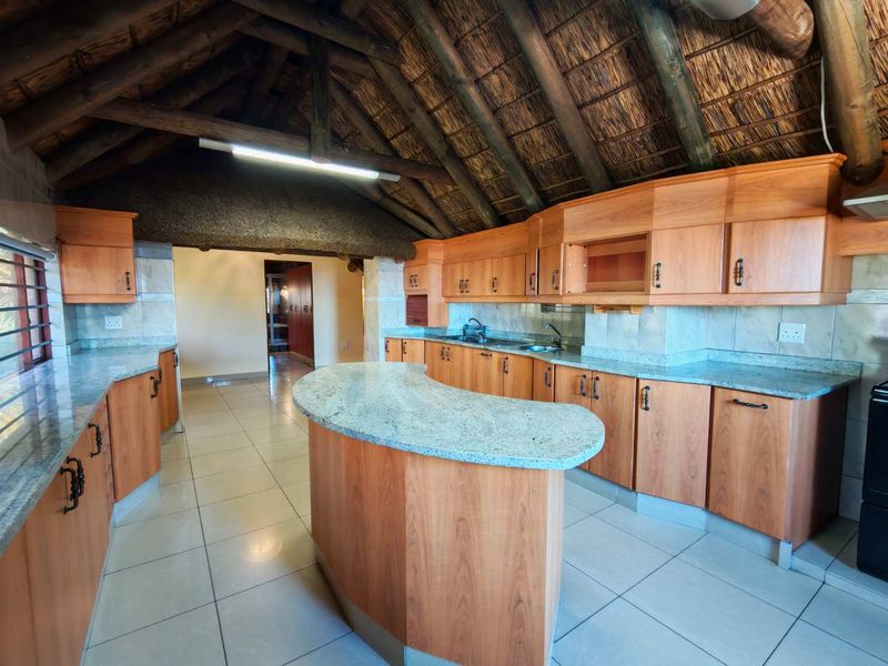 Spacious kitchen featuring wooden cabinetry, granite countertops, tiled flooring, and a unique exposed thatch roof with timber beams.