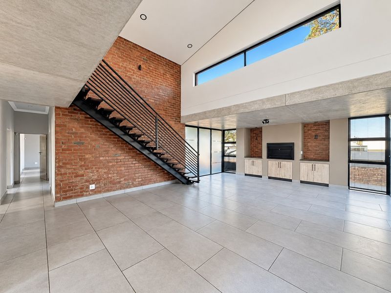 Spacious open-plan living area featuring exposed brick walls, a modern metal staircase, built-in cabinetry with a fireplace, and high clerestory windows.