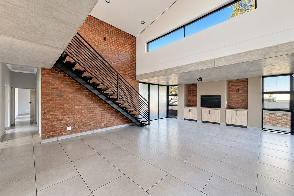 Spacious open-plan living area featuring exposed brick walls, a modern metal staircase, built-in cabinetry with a fireplace, and high clerestory windows.