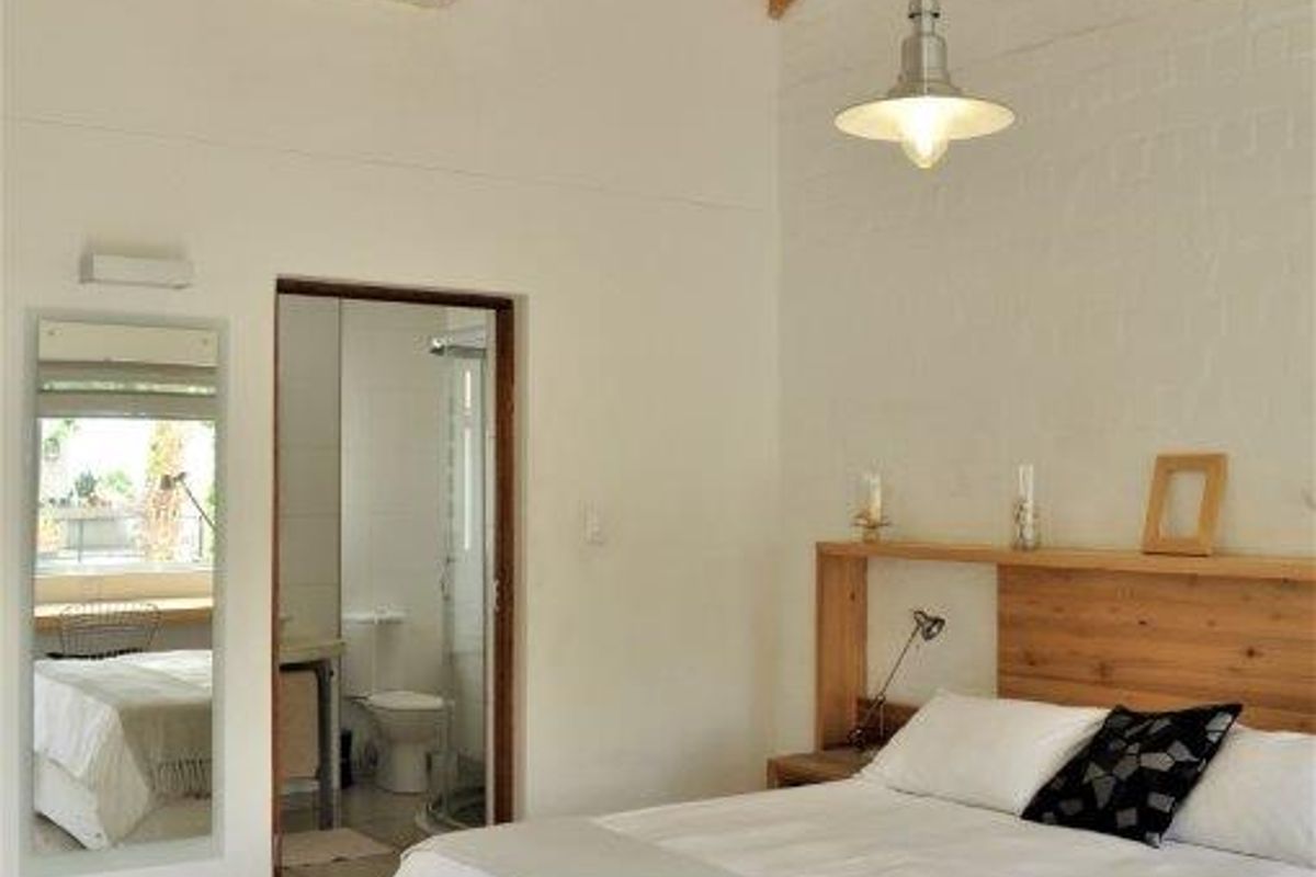 A bright bedroom featuring vaulted ceilings with exposed timber beams, tiled flooring, and an en-suite bathroom with a shower.