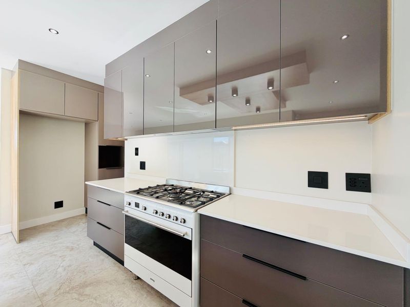 Modern kitchen featuring high-gloss cabinetry, stone countertops, a gas cooktop with oven, and sleek glass splashback with integrated lighting.
