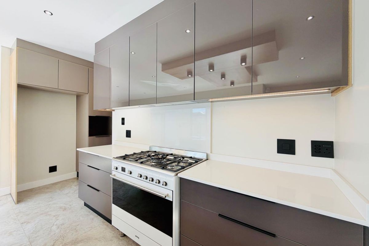 Modern kitchen featuring high-gloss cabinetry, stone countertops, a gas cooktop with oven, and sleek glass splashback with integrated lighting.