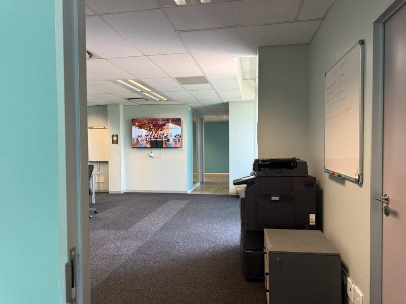 A functional office space featuring carpeted flooring, a suspended ceiling with recessed lighting, and integrated air conditioning vents.