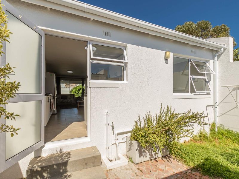 Rear exterior view of the property featuring a paved area, external access door, and aluminium window frames.