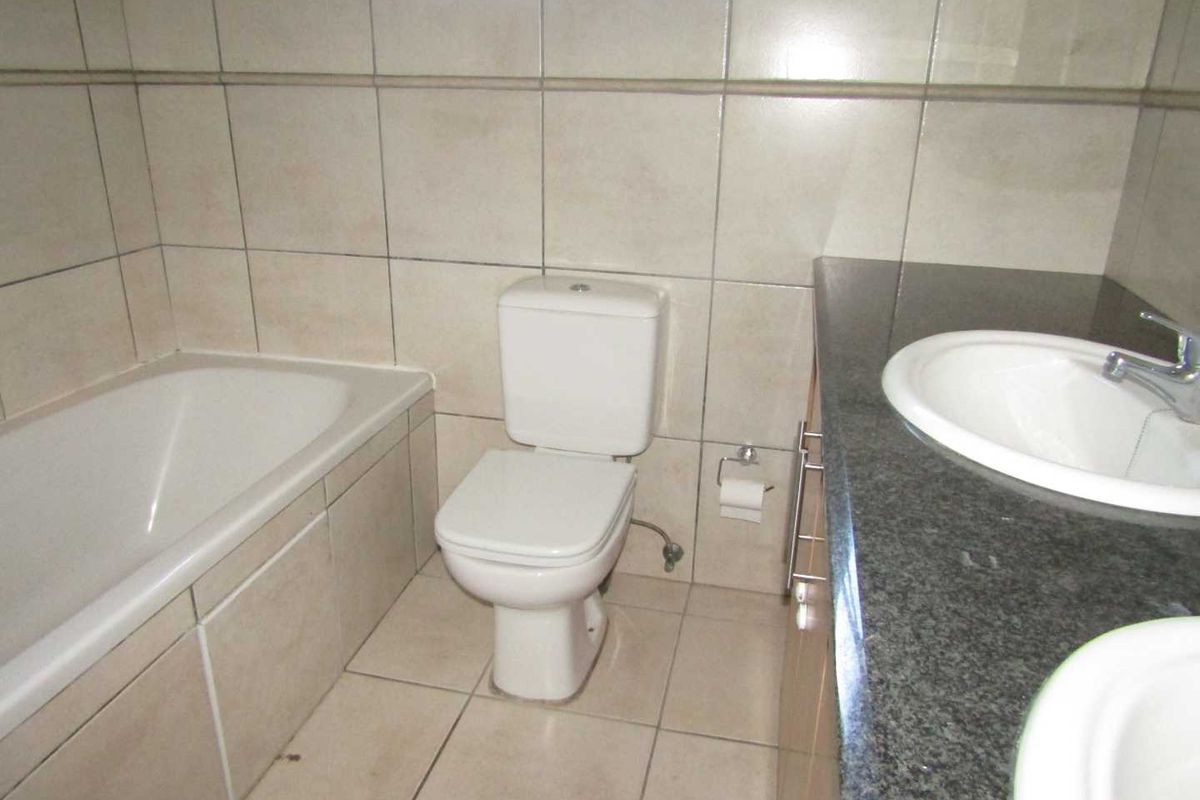 A functional bathroom featuring a built-in bathtub, a toilet, and a double vanity with a granite countertop and tiled finishes.