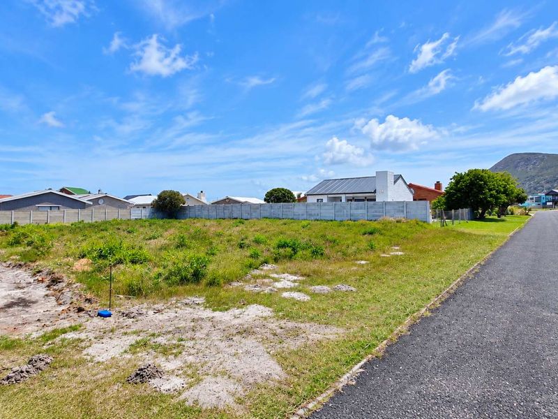 A vacant residential plot situated in a developed neighborhood, featuring level ground, boundary walling, and direct access to a paved street.