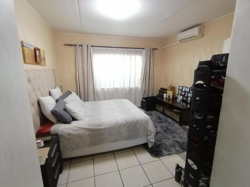 A bedroom featuring tiled flooring and a wall-mounted split-system air conditioner, providing a functional space with neutral wall tones.