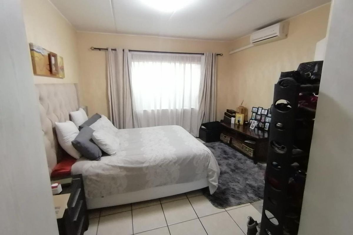 A bedroom featuring tiled flooring and a wall-mounted split-system air conditioner, providing a functional space with neutral wall tones.