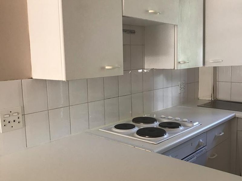 A compact kitchen featuring white built-in cabinetry, a four-plate electric hob, an integrated oven, and a tiled splashback.