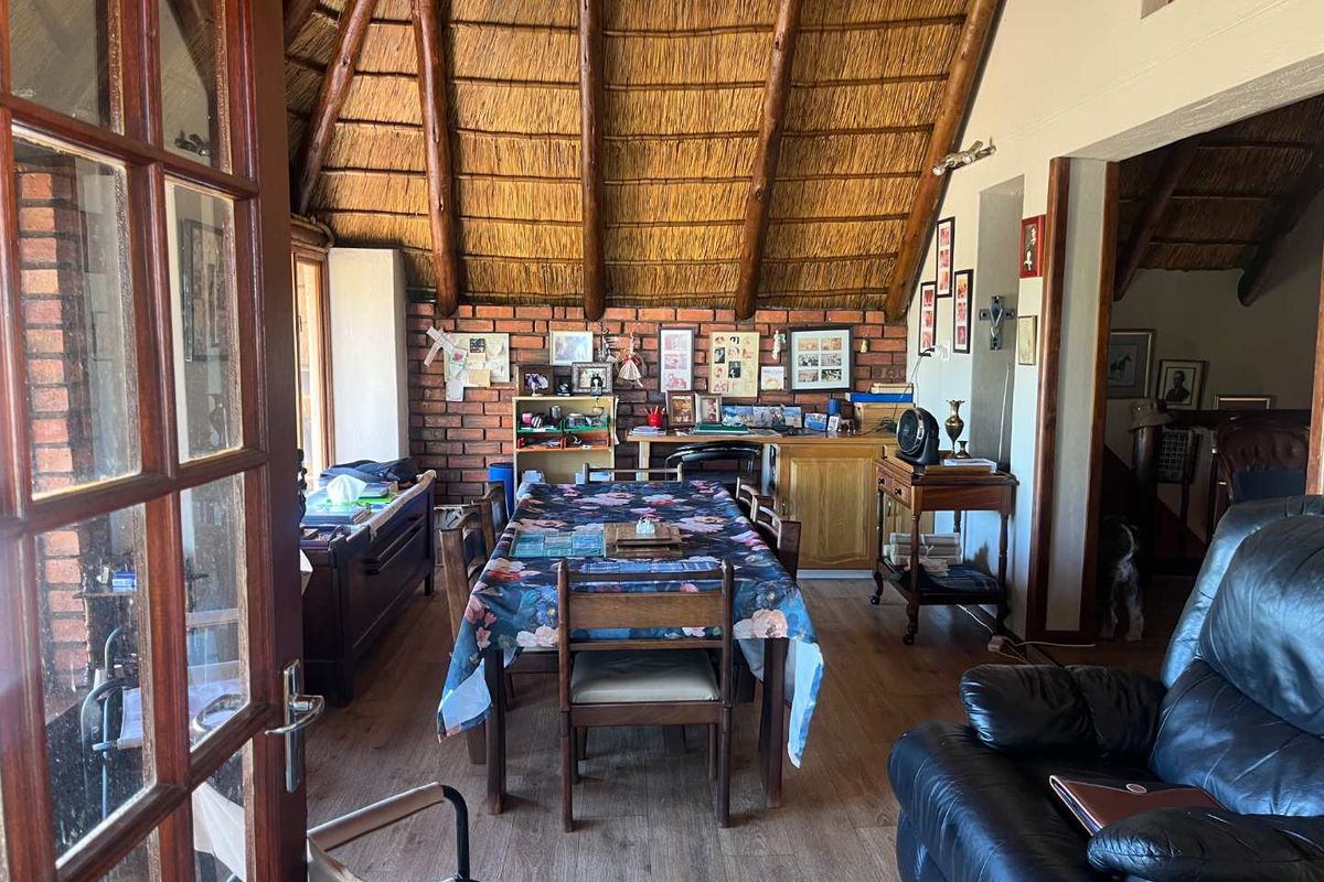 A living area featuring a rustic exposed thatch roof, exposed brick wall, and laminate flooring, offering a warm and character-filled atmosphere.