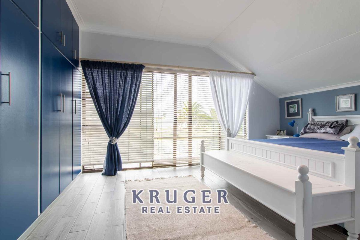 A well-maintained bedroom featuring built-in blue cabinetry, light-toned wood-look flooring, and large windows with blinds, offering a bright and clean living space.
