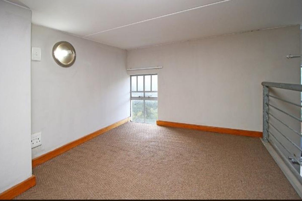 A carpeted loft area featuring a porthole window, a small rectangular window, and a metal safety railing overlooking the lower level.