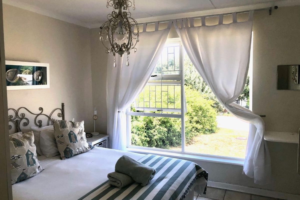 A bright bedroom featuring a large window with security bars, tiled flooring, and a decorative chandelier.