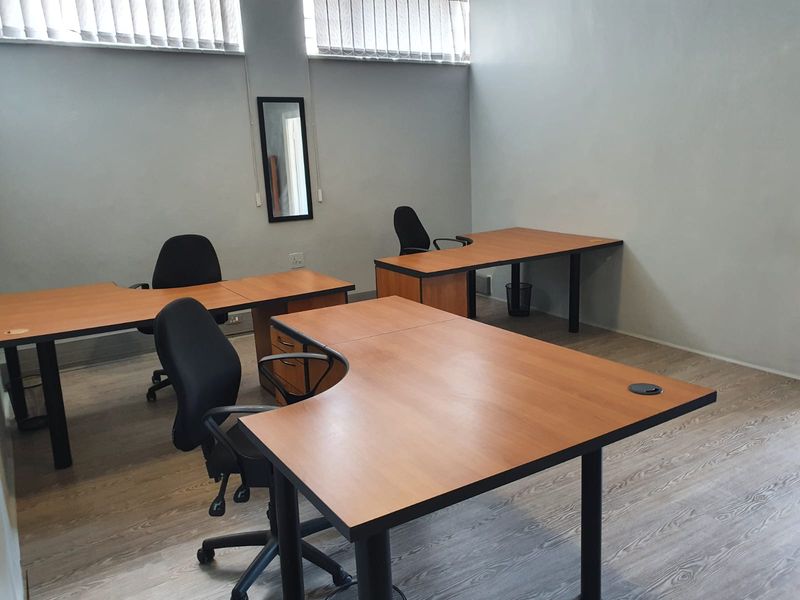 A functional office space featuring laminate flooring, neutral walls, and vertical window blinds, providing a clean and professional work environment.